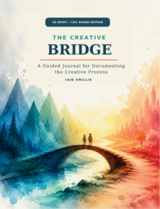 50-entry cover: The Creative Bridge 50-Entry Coil-Bound Edition cover featuring two figures crossing a watercolor bridge between cool blue and warm orange landscapes.